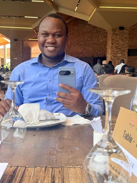 Brian at a restaurant table, phone in hand, smiling at the camera